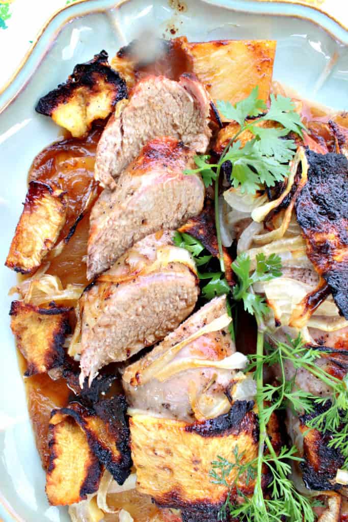 Vertical overhead closeup photo of a sliced pineapple pork tenderloin with onions and fresh cilantro.