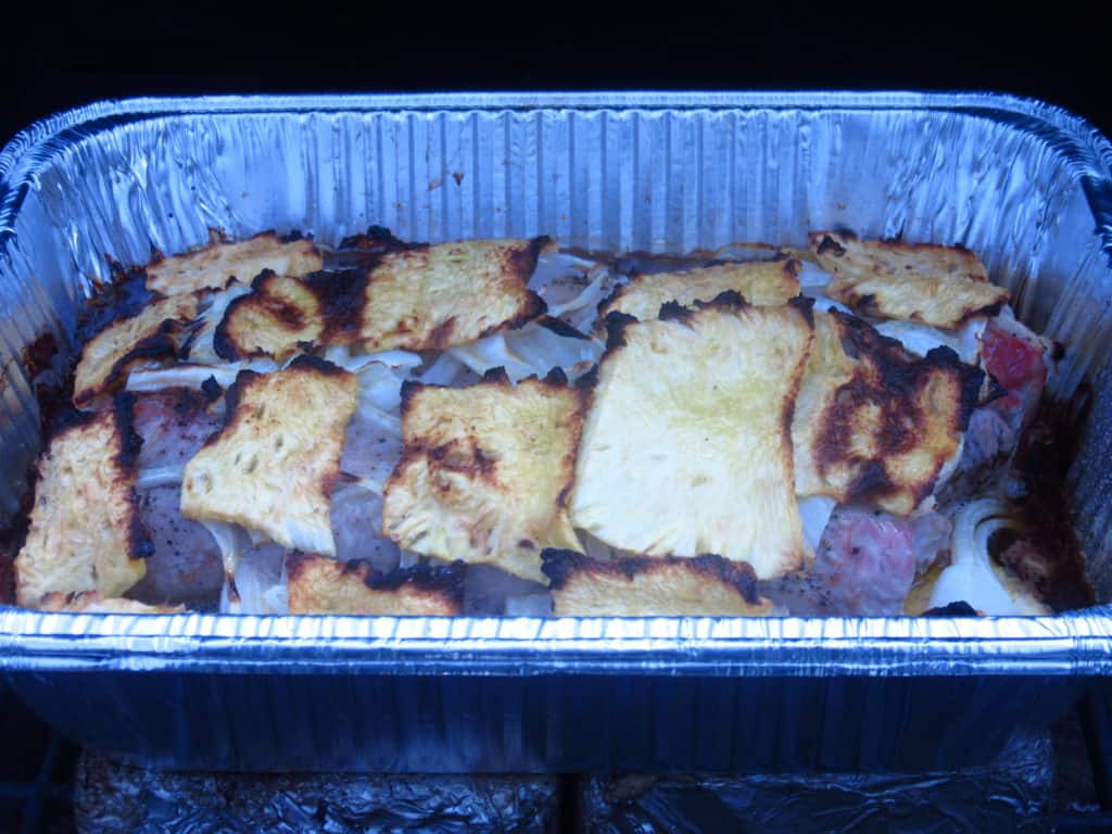 Pineapple pork tenderloin an an aluminum pan on an outdoor grill.