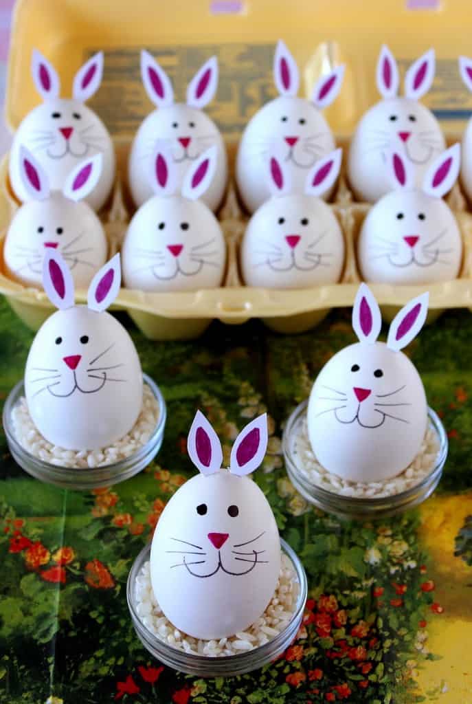 Vertical photo of a bunch of hard-boiled bunny eggs with pink noses, whiskers, and cute bunny ears.