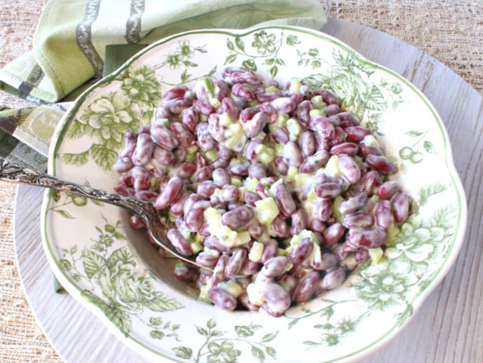 Overhead horizontal photo of creamy red bean salad in a green and white serving bowl with a serving spoon.
