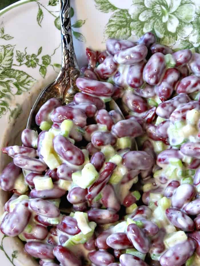 Vertical overhead close up image of a serving spoon dishing up a big helping of red bean salad with green onion and celery.