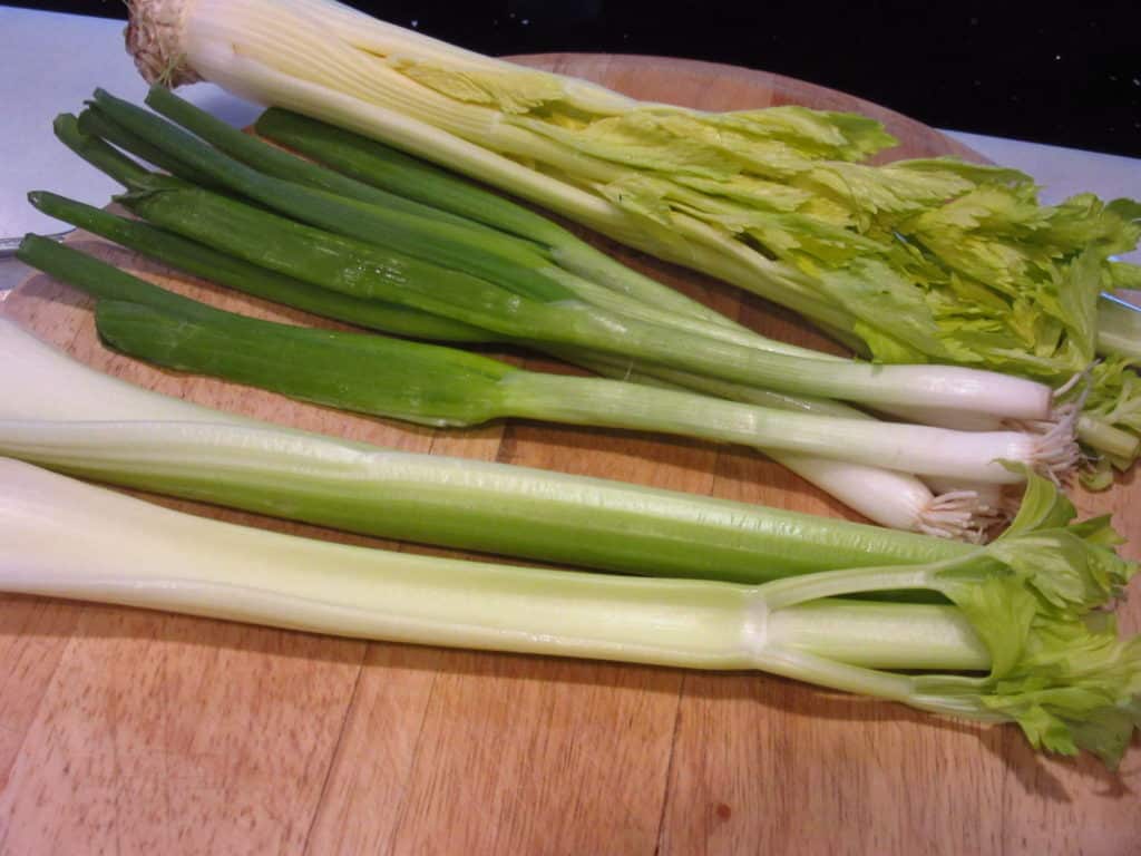 Green onions and celery on a cutting board.