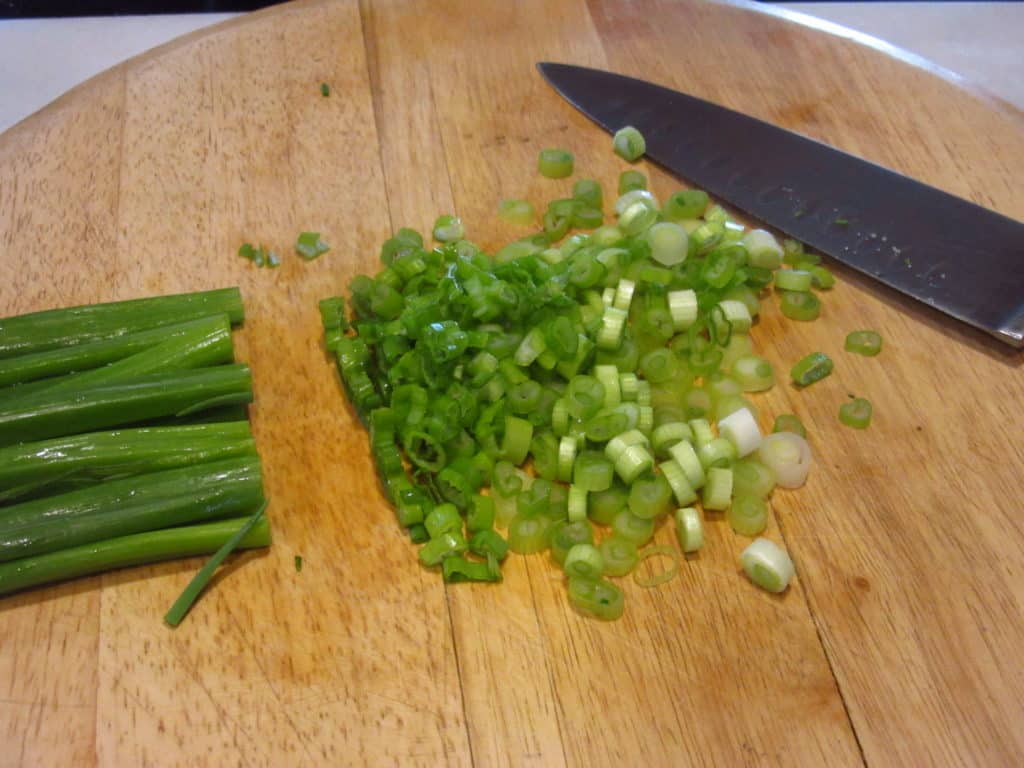 Chopped scallions on a wooden cutting board.