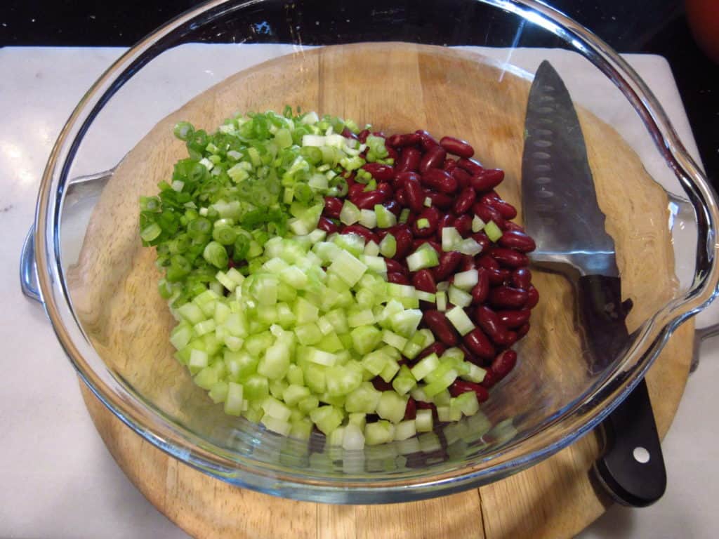 Scallions, celery and kidney beans in a glass bowl.