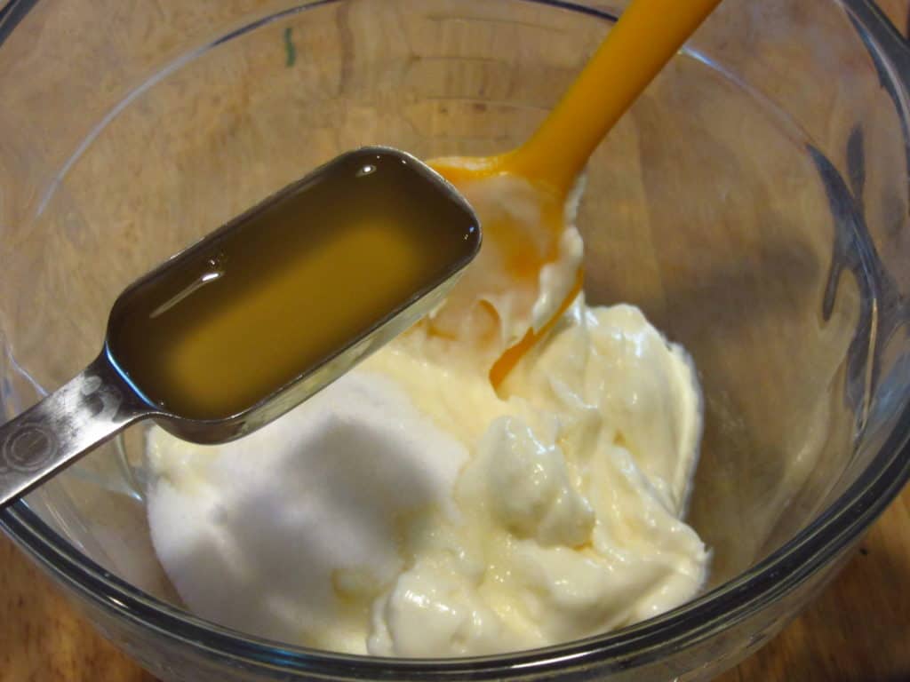 A teaspoon of apple cider vinegar being added to a dressing.