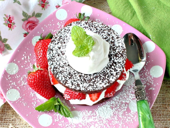 Overhead photo of a round brownie filled with whipped cream and strawberries on a pink polka dot plate.