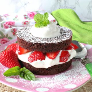 A colorful photo of a brownie strawberry shortcake on a pink polka dot plate with fresh strawberries and mint.