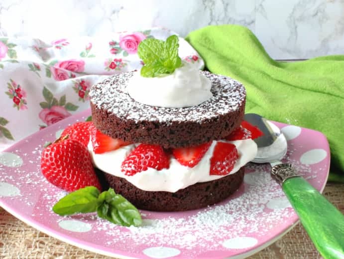 A colorful photo of a brownie strawberry shortcake on a pink polka dot plate with fresh strawberries and mint.