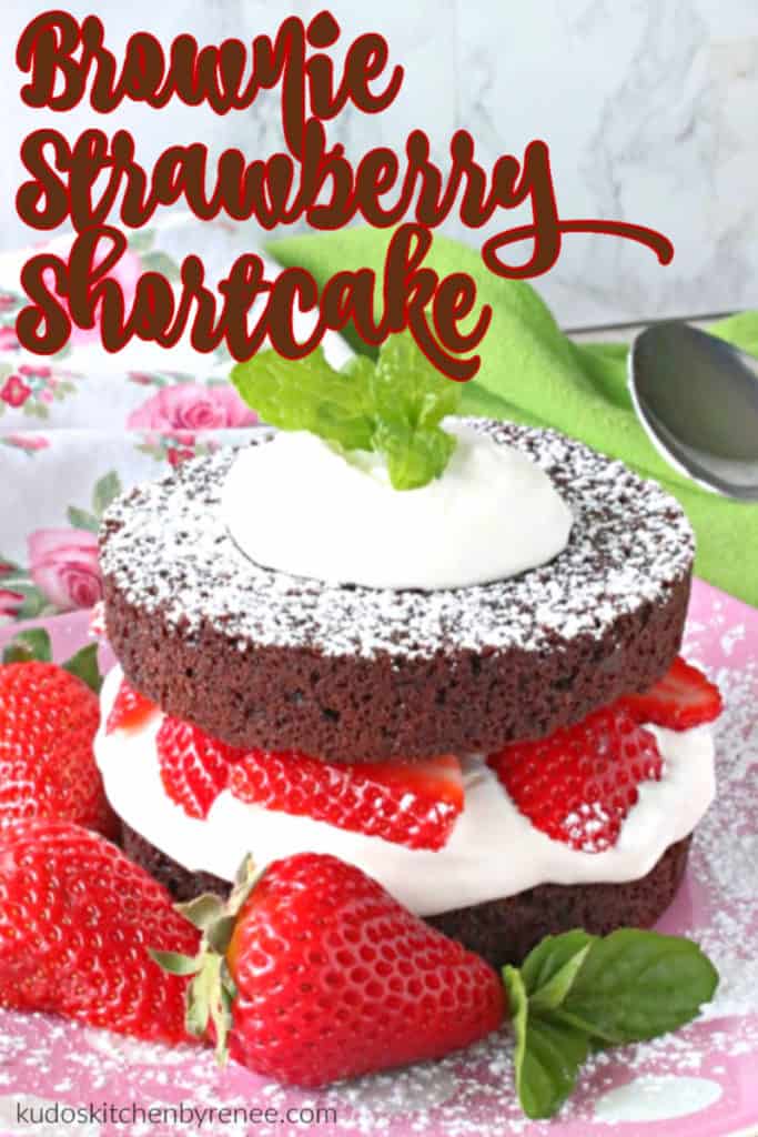 A closeup vertical image of a brownie strawberry shortcake with whipped cream, fresh strawberries and mint leaves.