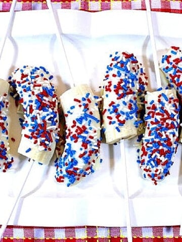 An overhead photo of a white plate filled with White Chocolate Covered Frozen Bananas with red and blue sprinkles.