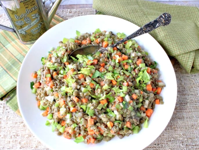 Overhead photo of French lentil salad in a large white bowl with a serving spoon and an olive oil bottle in the background.