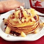 A stack of sweet potato pancakes topped with diced apples and chopped pecans.