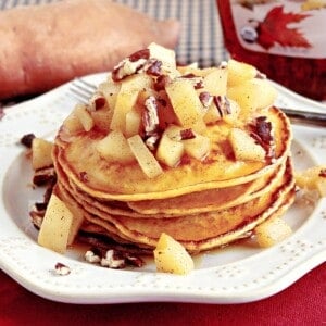 A stack of sweet potato pancakes topped with diced apples and chopped pecans.