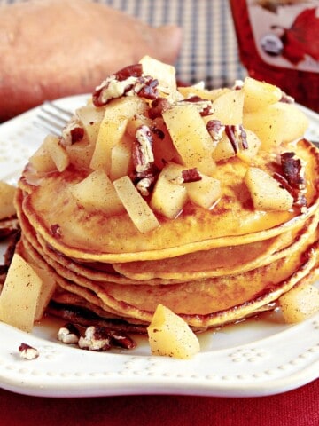 A stack of sweet potato pancakes topped with diced apples and chopped pecans.