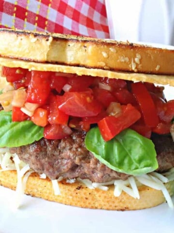A Bruschetta Burger on a white plate with tomatoes and basil.