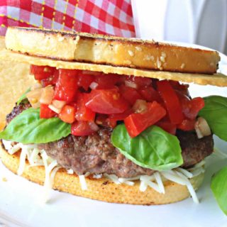 A Bruschetta Burger on a white plate with tomatoes and basil.