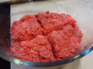 Scored ground beef in a glass bowl.