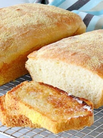 Two loaves of English muffin bread, one sliced and toasted on a wire rack with a blue and brown napkin in the background.