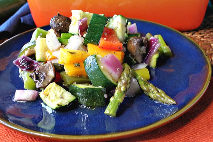 A closeup photo of roasted summer vegetables bell peppers, asparagus, mushrooms, zucchini, and summer squash on a blue plate.