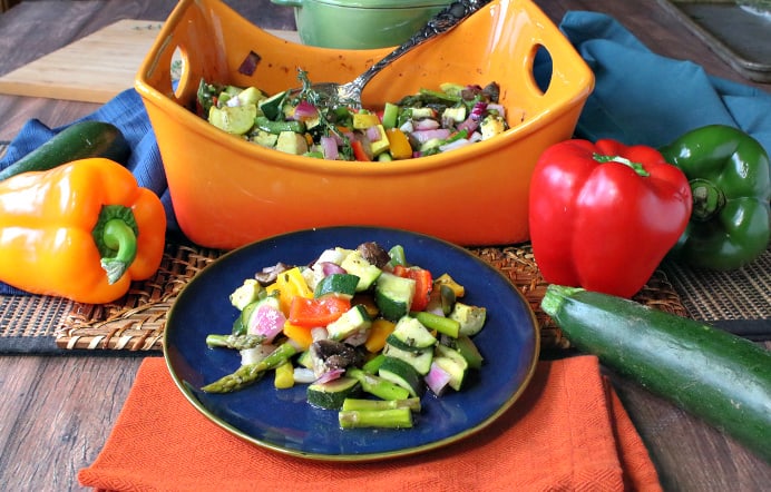 A plate of roasted summer vegetables on a blue plate with a casserole dish in the background. For a bbq side dish recipes roundup