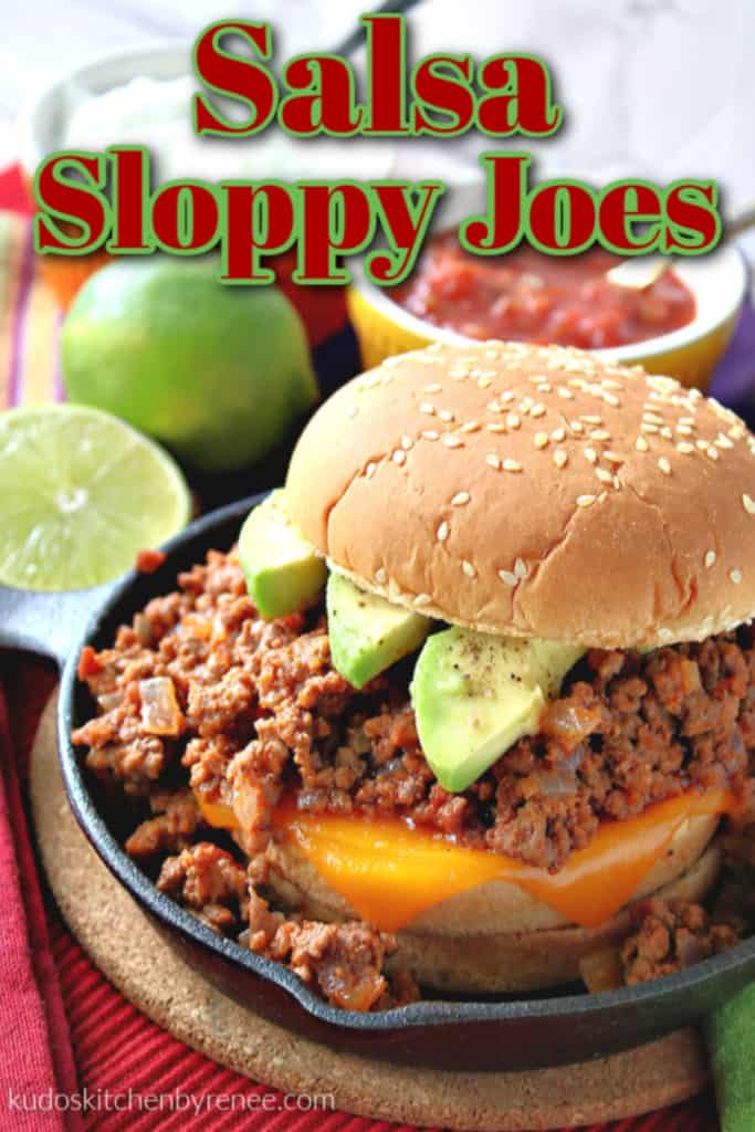 Closeup vertical image of a salsa sloppy joes sandwich in a cast iron skillet with melted cheese and avocado slices on a bun.