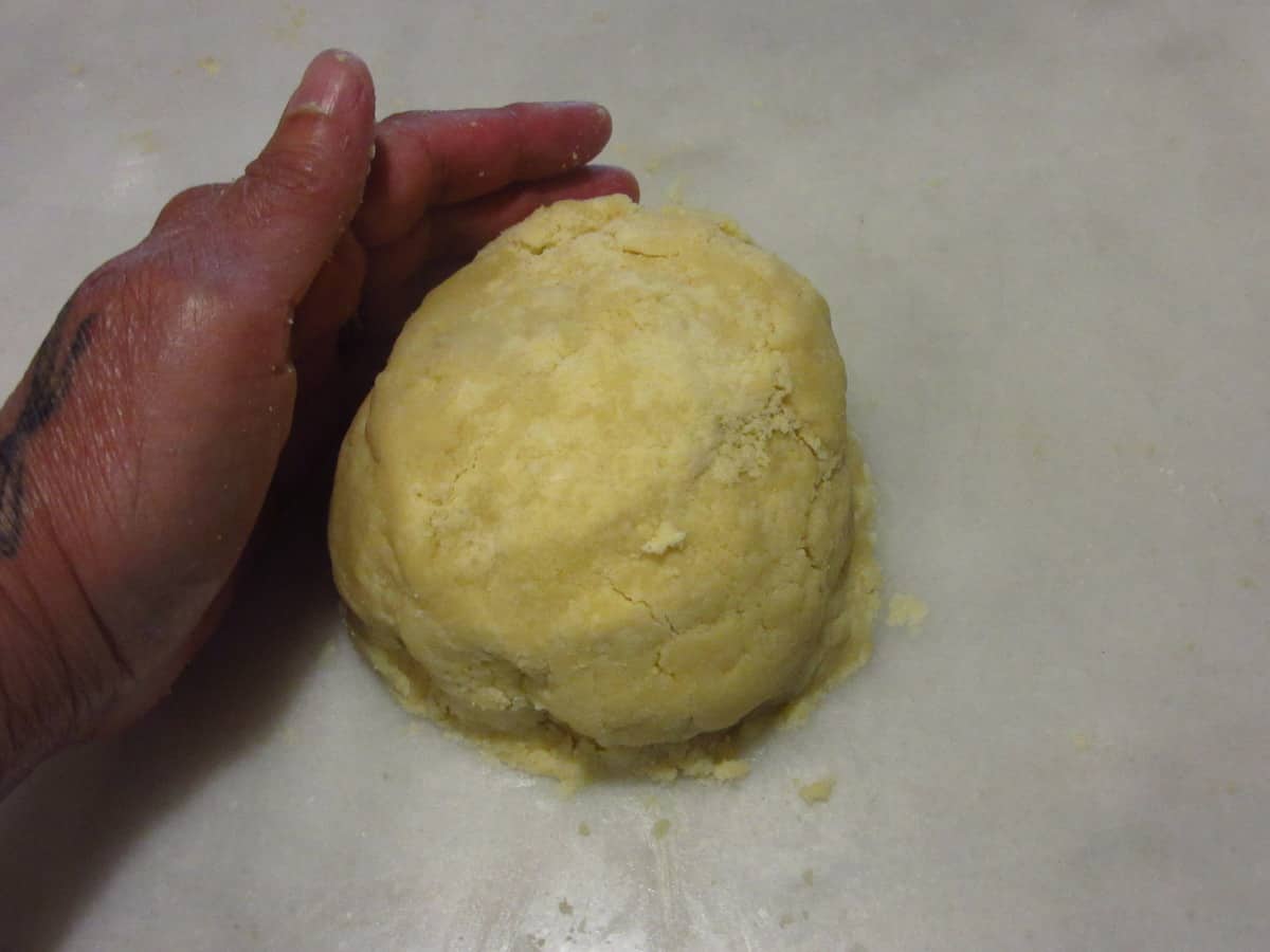 A hand forming a round ball of pie dough.