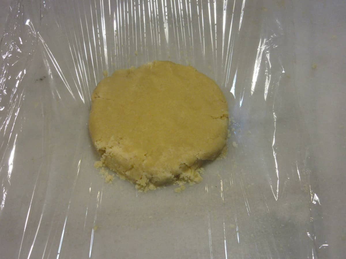 A round disc of pie dough being wrapped for chilling.