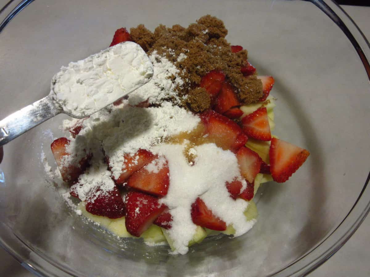 Flour being added to a pie filling in a bowl.