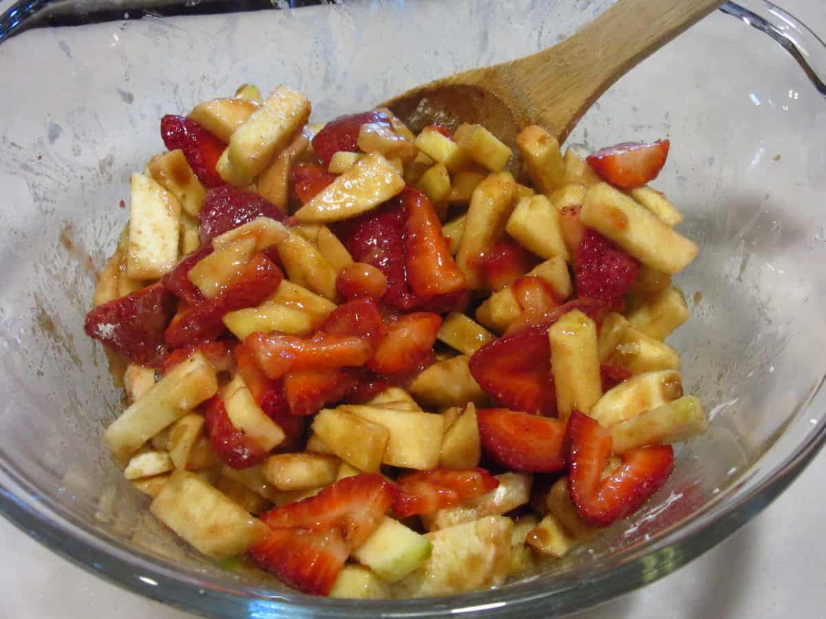 A mix of apples and strawberries in a bowl with spices to make a pie.