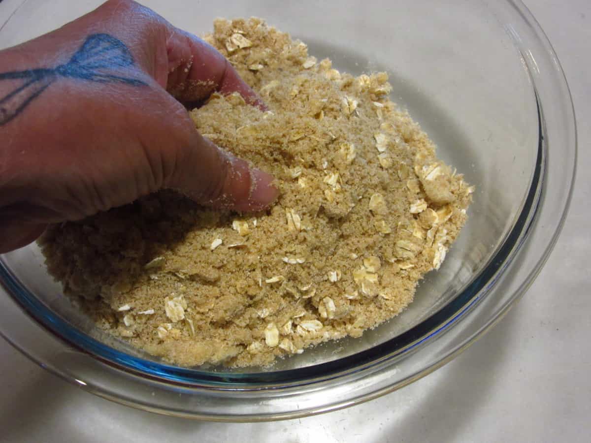 A hand mixing up streusel topping for a pie.