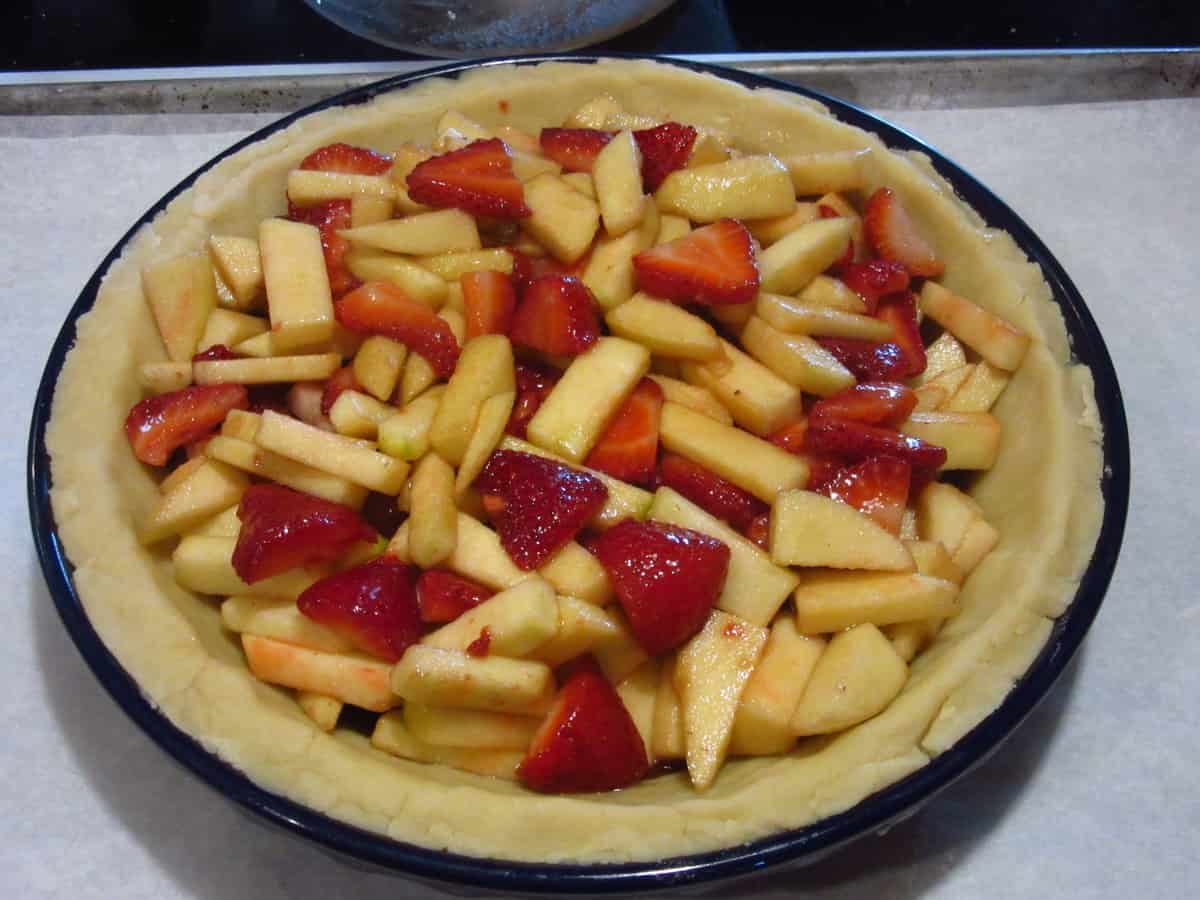 Apples and strawberries inside a pie shell for a pie.