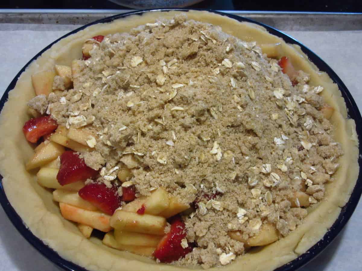 A streusel topping being added to an apple and strawberry pie.