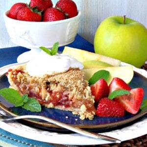 A pretty slice of Streusel Topped Strawberry Apple Pie with whipped cream and mint on top.