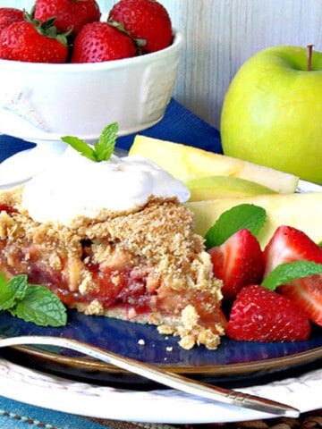 A slice of Strawberry Apple Pie on a blue plate with mint as garnish.