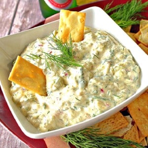 A white square bowl filled with Cucumber Dill Dip along with two crackers.