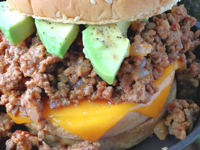Super closeup photo of a salsa sloppy joes sandwich with melted cheese, avocado slices, salt and pepper on a sesame seed bun.