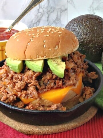 A salsa sloppy joe sandwich in a small cast iron skillet with avocado slices and a sesame seed bun.