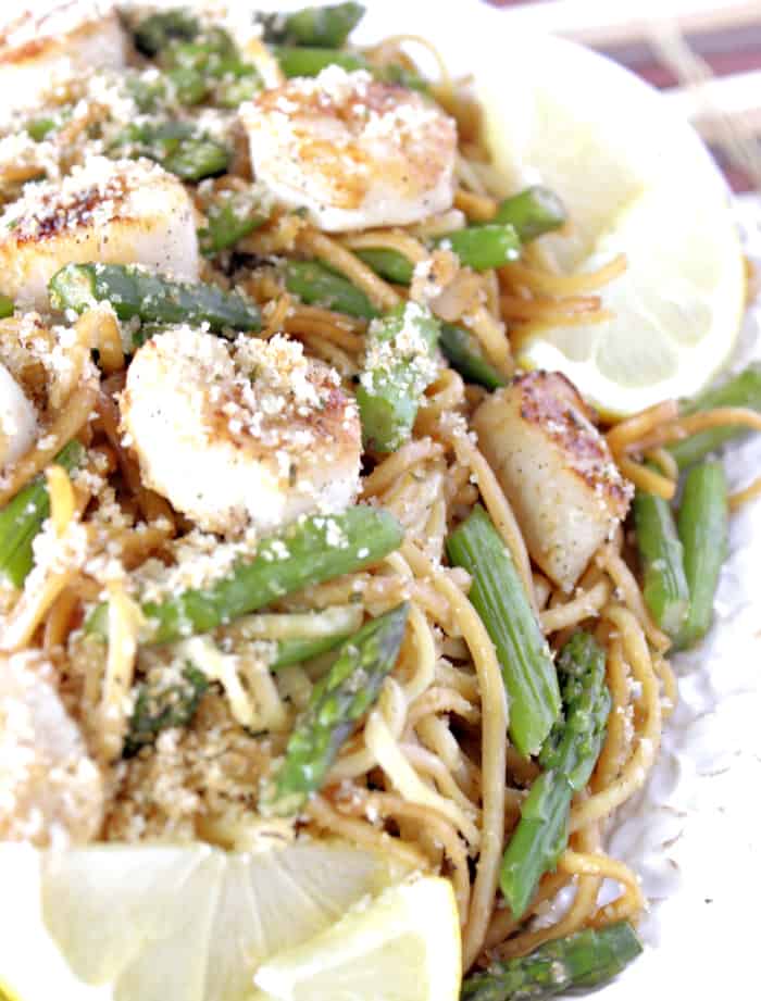 Super closeup photo of seared scallops with linguine and asparagus on a platter with lemon and toasted breadcrumbs.