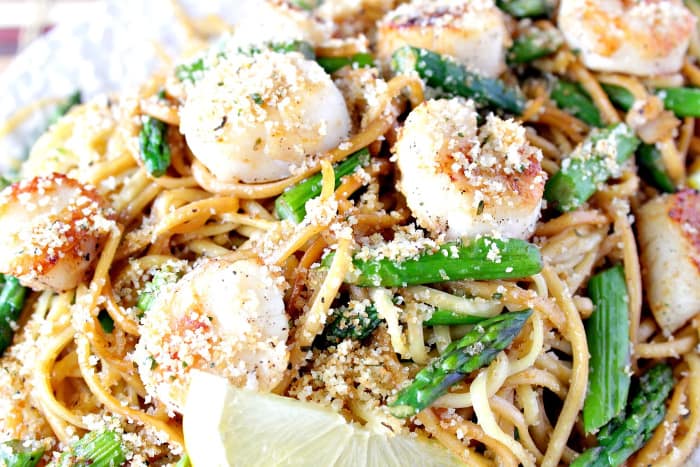 A closeup horizontal photo of Seared Scallops with Linguine and Asparagus with a lemon slice.