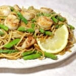 A plate of Scallops with Linguine and Asparagus along with a slice of lemon.