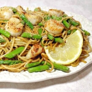 A plate of Scallops with Linguine and Asparagus along with a slice of lemon.