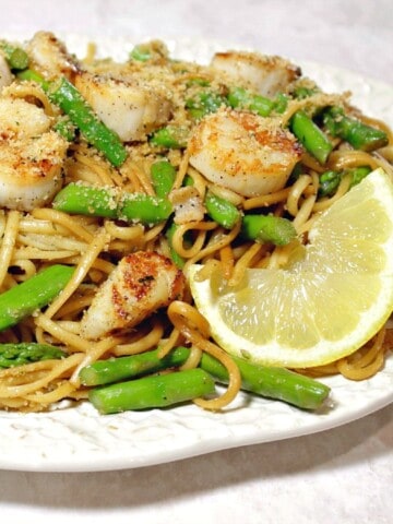 A plate of Scallops with Linguine and Asparagus along with a slice of lemon.