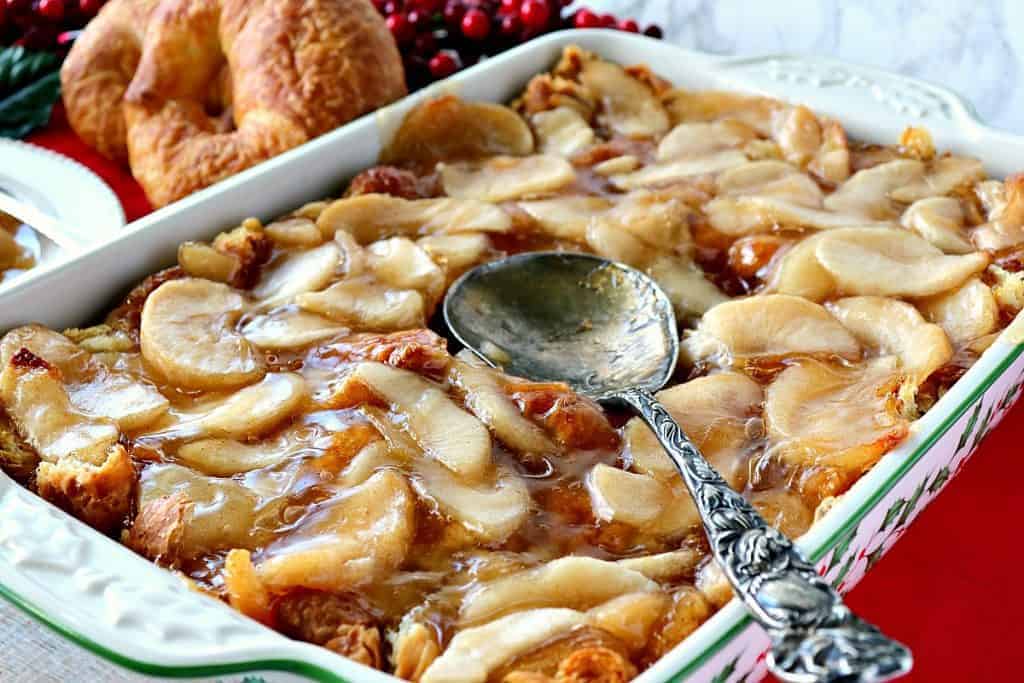 A casserole dish filled with apple croissant breakfast bake with a serving spoon.