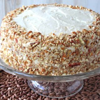 An entire banana poppy seed cake covered in pecans on a glass cake plate.