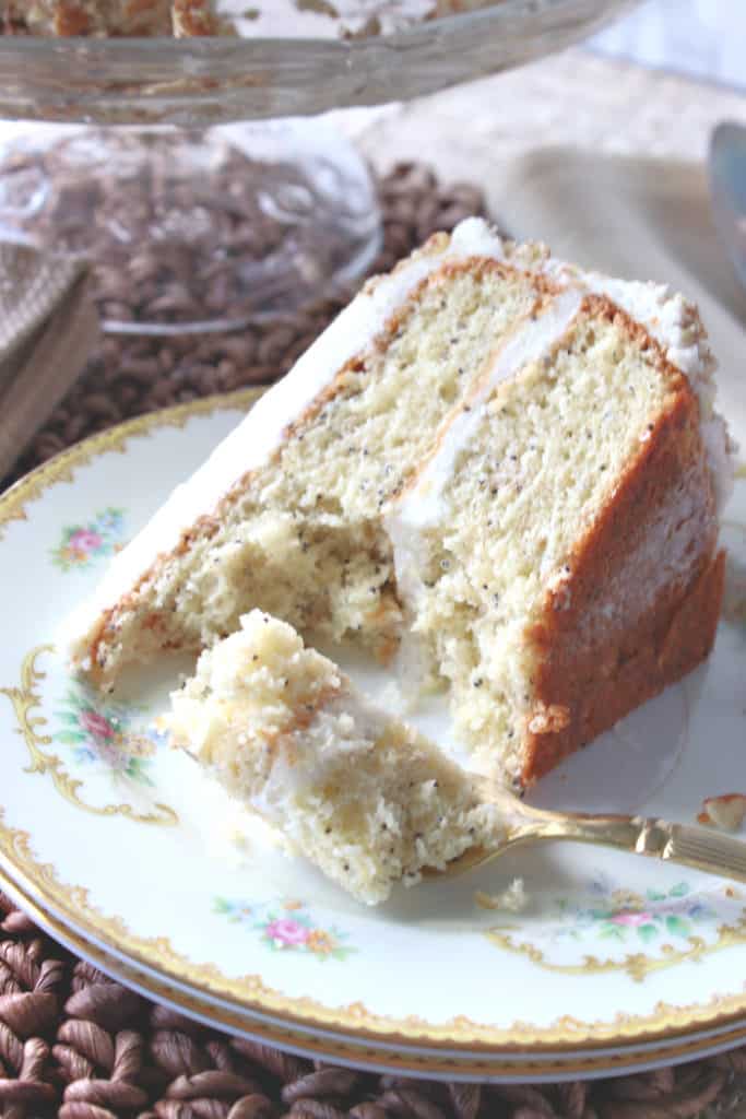 A vertical image of a slice of banana poppy seed cake on a pretty plate with a gold fork with a piece of cake on it.