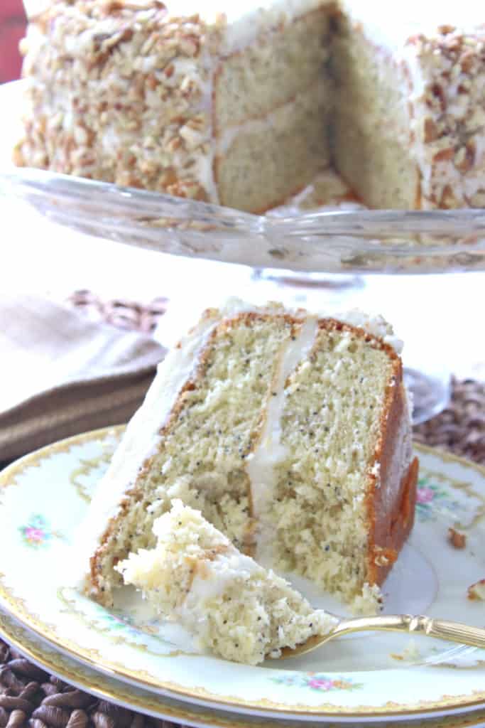 A vertical closeup of a slice of banana poppy seed cake on a pretty plate with the whole cake in the background.