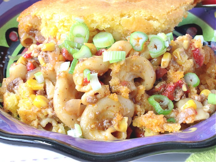 A super closeup photo of a bowlful of chili mac casserole with scallions, pasta, ground beef, corn, and red pepper.