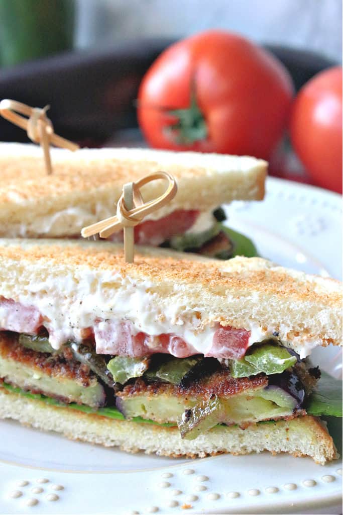 A vertical closeup photo of a fried eggplant sandwich with mayo, green bell pepper, and tomato on toast and a toothpick. How to make a fried eggplant sandwich.
