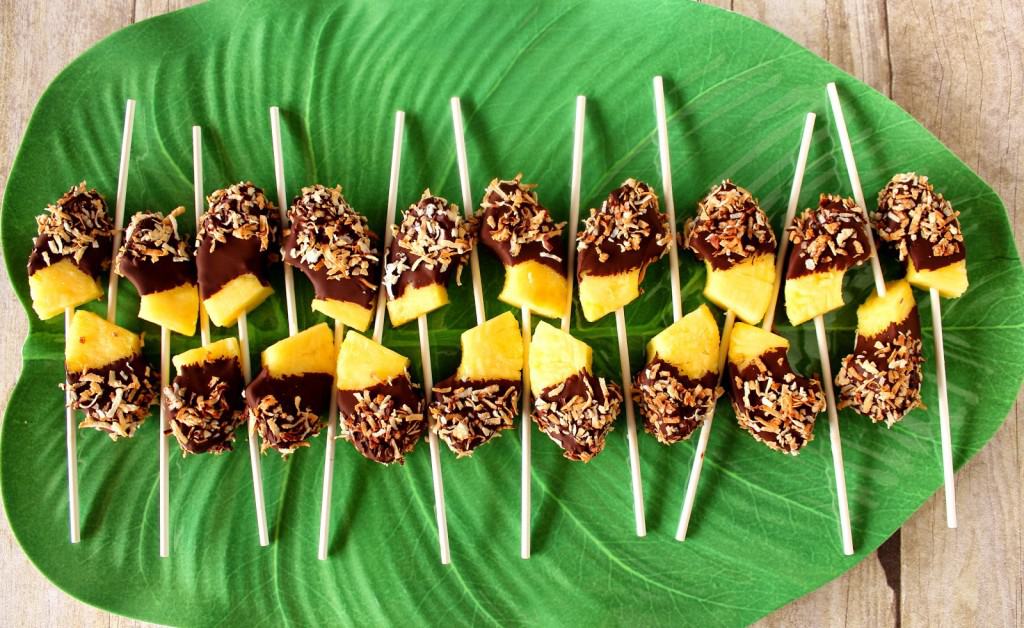 A tropical green leaf plate lined up with frozen pineapple pops with chocolate and toasted coconut.