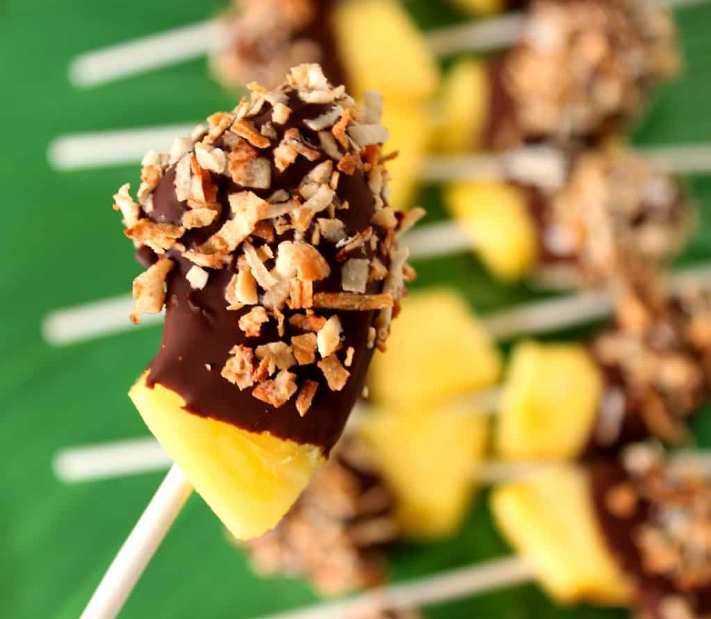 A closeup photo of a frozen pineapple pop on a stick with chocolate and toasted coconut.